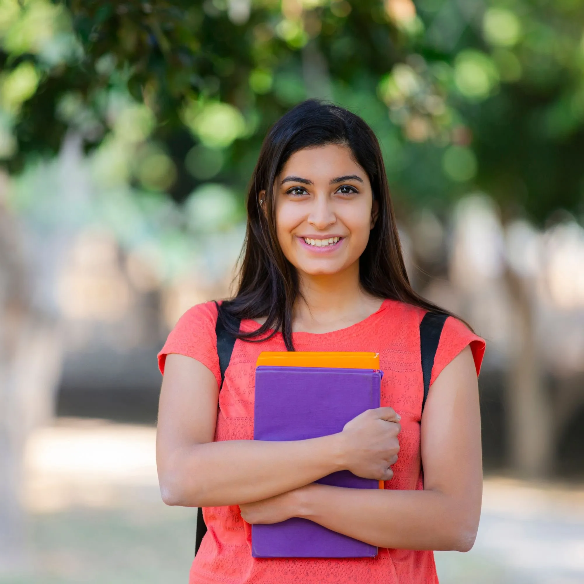 A smiling student holding her books outside school, backpack on her shoulders