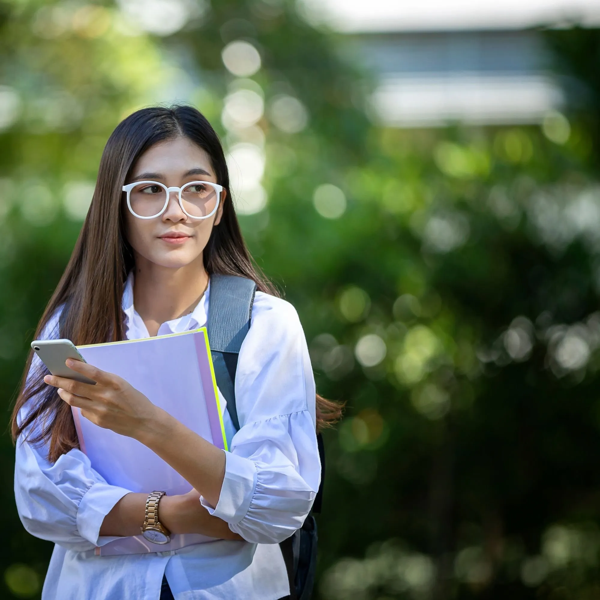 A confident student with glasses holding her notebooks outdoors